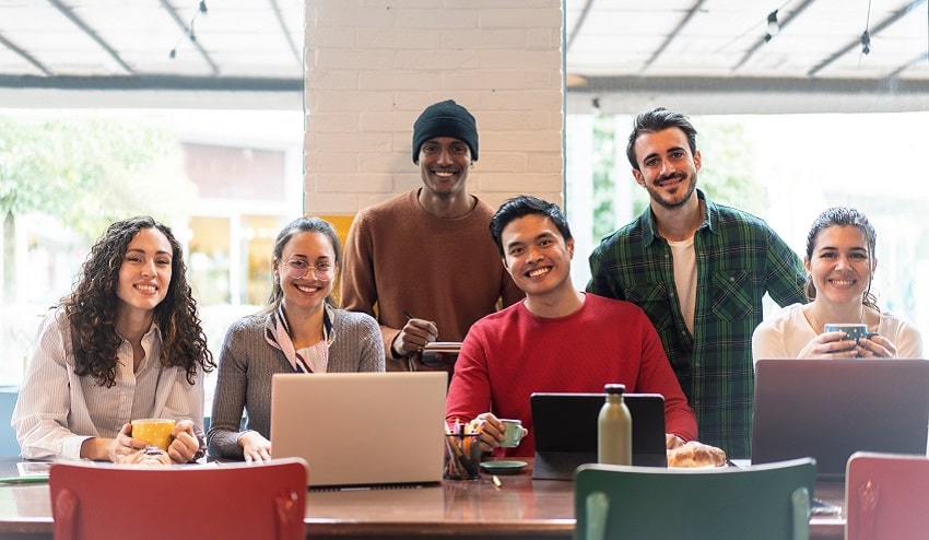 Smiling multiethnic coworkers looking at camera making team picture in modern office together - Happy diverse work group or department laugh posing for photo at workplace